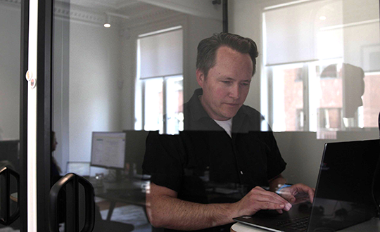 Close-up view of a man working on a laptop inside a glass meeting pod